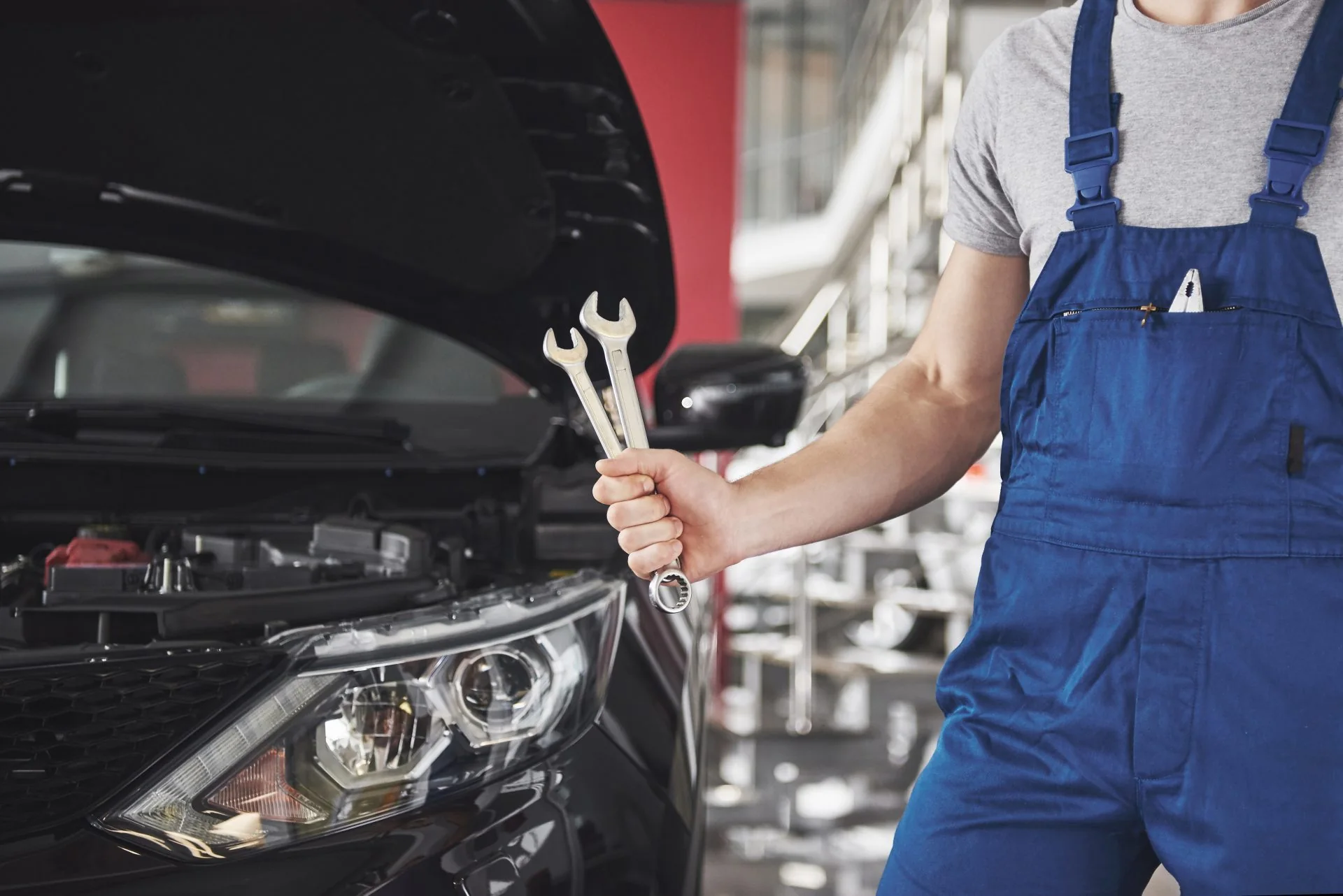 Mechanik s klíčem před vozem s otevřenou kapotou