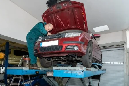 Mechanik pracuje pod otevřenou kapotou vozu na zvedáku